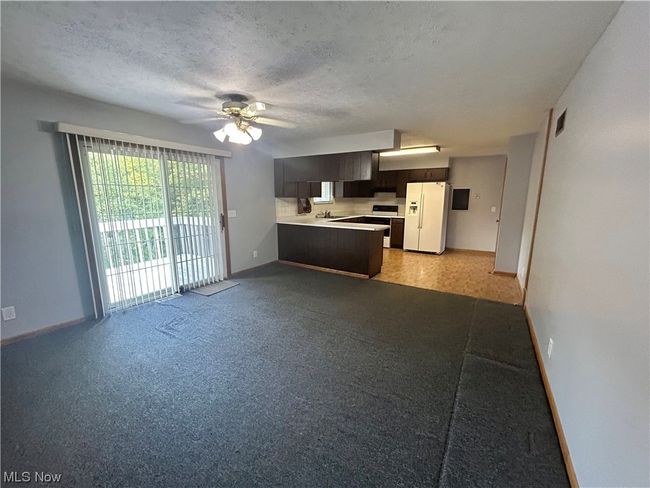 Kitchen with light colored carpet, ceiling fan, stove, white fridge with ice dispenser, and sink | Image 9