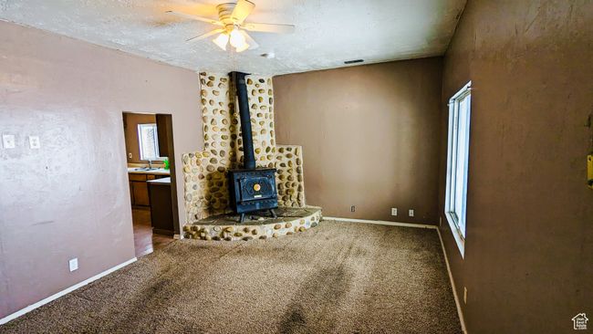 Unfurnished living room featuring carpet flooring, a wood stove, ceiling fan, sink, and a textured ceiling | Image 31