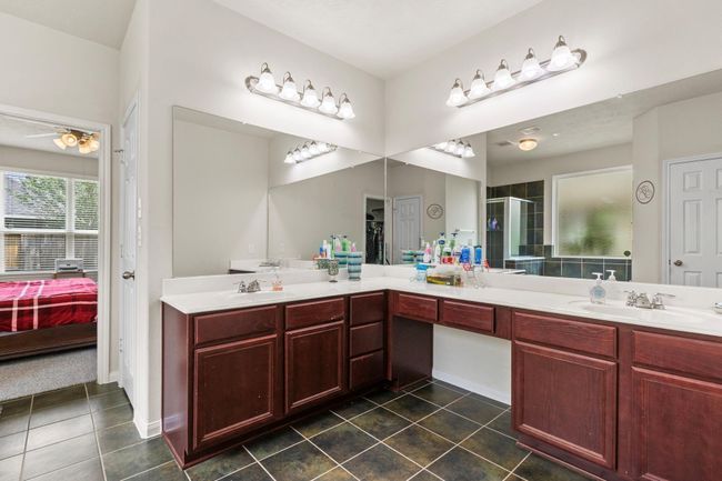 This spacious bathroom features dual sinks with dark wood cabinetry, large mirrors, and modern lighting. It connects to a bedroom with natural light and has a tiled floor for easy maintenance. | Image 17