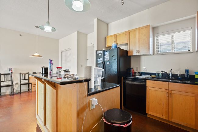 Kitchen with black appliances, dark countertops, a sink, and concrete floors | Image 5