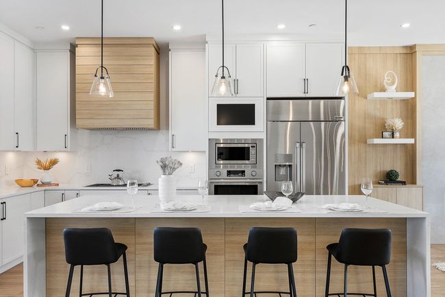 Kitchen with stainless steel appliances, a kitchen island, white cabinets, premium range hood, and light stone countertops | Image 5