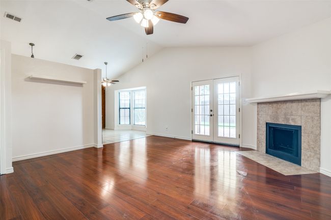 Unfurnished living room with ceiling fan, lofted ceiling, wood finished floors, a tiled fireplace, and french doors | Image 6