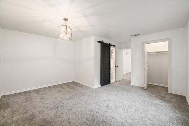 Unfurnished bedroom with carpet floors, a barn door, baseboards, a chandelier, and a closet | Image 13