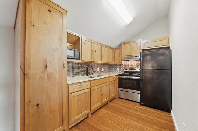 Kitchen featuring black appliances, a sink, under cabinet range hood, light brown cabinetry, and light wood-style floors | Image 36