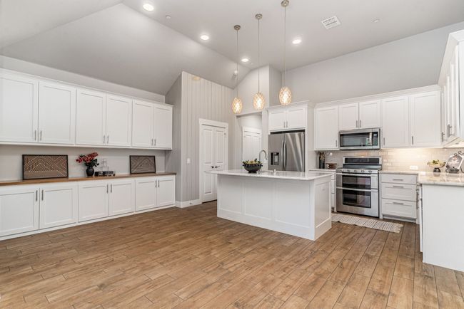Kitchen featuring stainless steel appliances, high vaulted ceiling, white cabinetry, decorative backsplash, and hanging light fixtures | Image 10