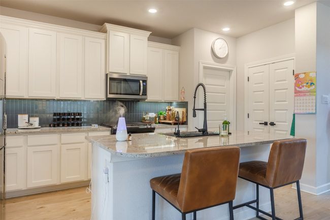 Kitchen with stainless steel microwave, decorative backsplash, white cabinetry, light stone countertops, and light wood-style flooring | Image 8