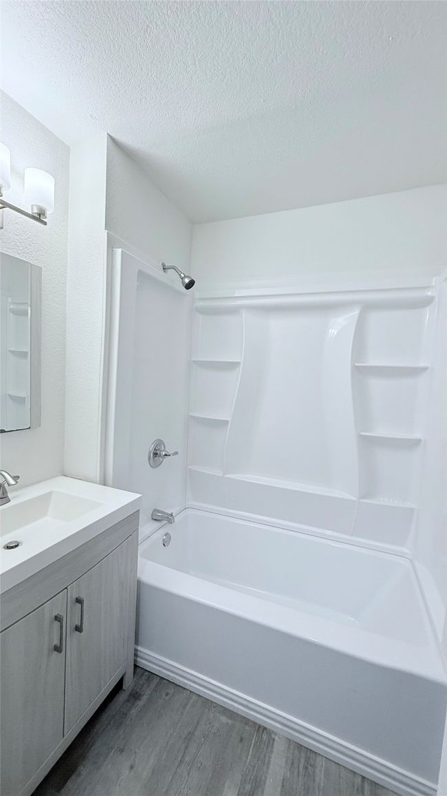 Full bath featuring wood finished floors, vanity, a textured ceiling, and washtub / shower combination | Image 10