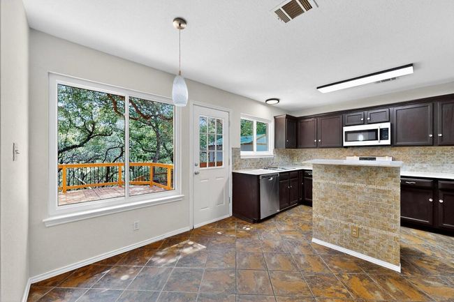 Kitchen with stainless steel dishwasher, light countertops, dark brown cabinets, decorative backsplash, and baseboards | Image 11