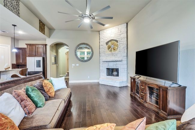 Living area with arched walkways, ceiling fan, dark wood-style flooring, and a limestone fireplace | Image 19