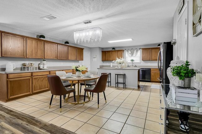 Kitchen with light tile patterned floors, light countertops, stainless steel dishwasher, brown cabinets, and a chandelier | Image 6