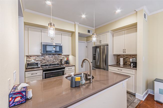 Kitchen with stainless steel appliances, wood finished floors, hanging light fixtures, tasteful backsplash, and crown molding | Image 11