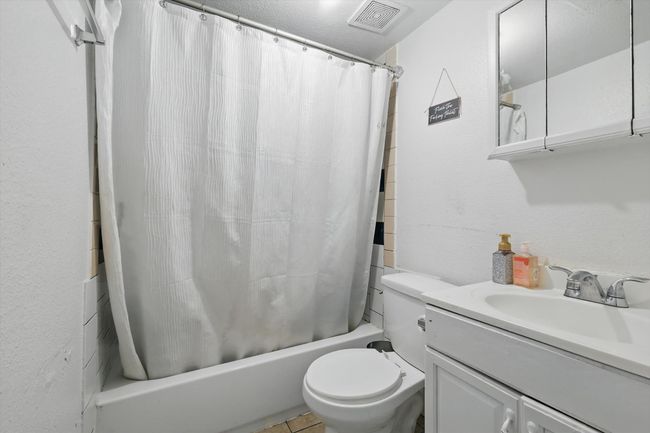 Bathroom with a textured wall, vanity, shower / tub combo with curtain, toilet, and visible vents | Image 11