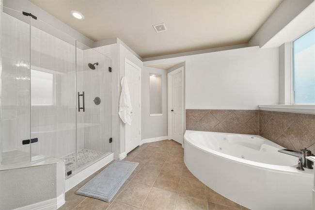 Relax and unwind in the updated and over-sized tile surrounded and frameless glass enclosed shower with seating (2021) and nearby whirlpool tub with privacy glass window above. Additional features include a linen storage closet, private water closet and a 14' walk-in wardrobe storage closet. | Image 26
