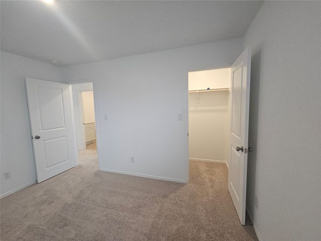 Unfurnished bedroom featuring a walk in closet, light colored carpet, a closet, and baseboards | Image 7