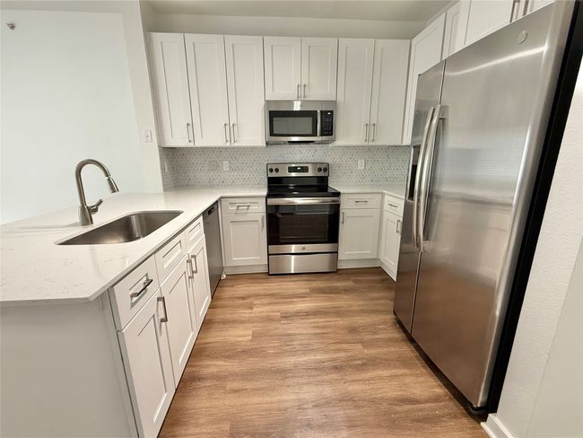 Kitchen featuring appliances with stainless steel finishes, a sink, a peninsula, light wood-style flooring, and backsplash | Image 5