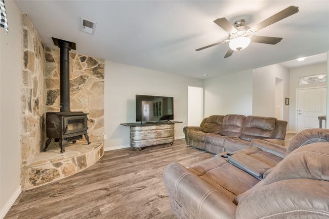 Living area with baseboards, a wood stove, visible vents, ceiling fan, and wood finished floors | Image 10
