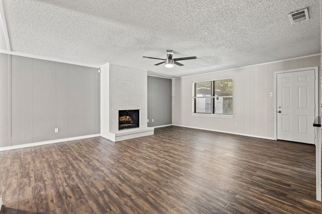 Unfurnished living room with ceiling fan, dark wood-type flooring, a brick fireplace, crown molding, and a textured ceiling | Image 10