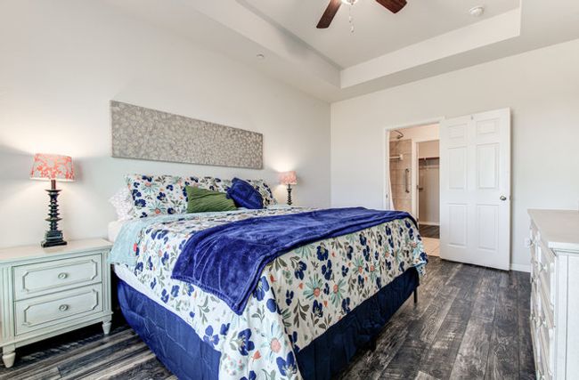 Bedroom with dark wood-type flooring, a raised ceiling, a walk in closet, and a ceiling fan | Image 9