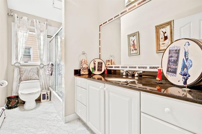 Bathroom featuring vanity, toilet, marble look tiles, baseboard heating, and shower / bath combination with glass door | Image 32