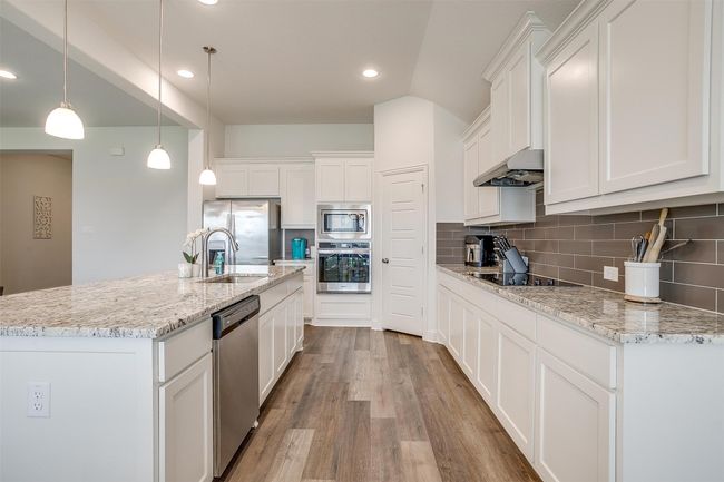 Kitchen featuring stainless steel appliances, under cabinet range hood, light wood-style floors, white cabinets, and backsplash | Image 13