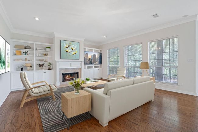 A large den with a fireplace with flush hearth, crown molding, ceiling fan, and views of the greenbelt from inside. (virtually staged) | Image 6