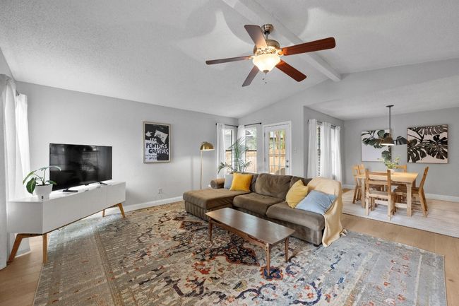 Living and dining areas featuring lots of natural light, a ceiling fan, a tiled wood-burning fireplace, engineered wood floors, with door to deck and backyard. | Image 6