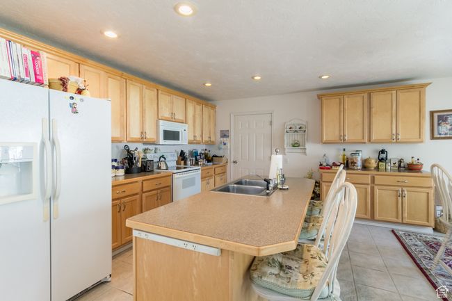 Kitchen with recessed lighting, a kitchen island with sink, white appliances, a sink, and light tile patterned flooring | Image 8