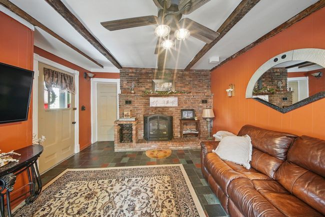 Living area featuring ceiling fan, beamed ceiling, a fireplace, and stone tile floors | Image 6