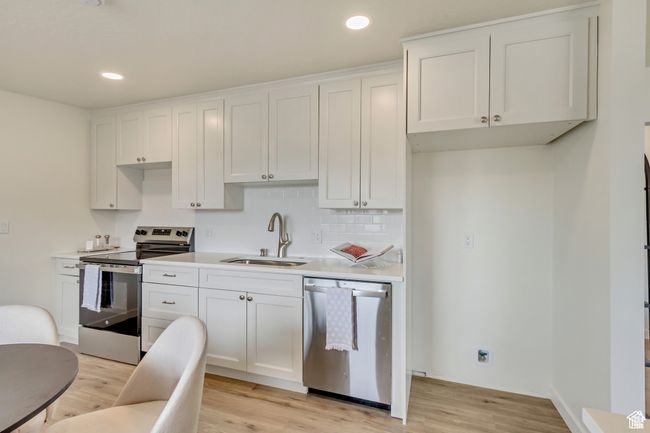 Kitchen with appliances with stainless steel finishes, a sink, white cabinetry, and light wood-style floors | Image 9