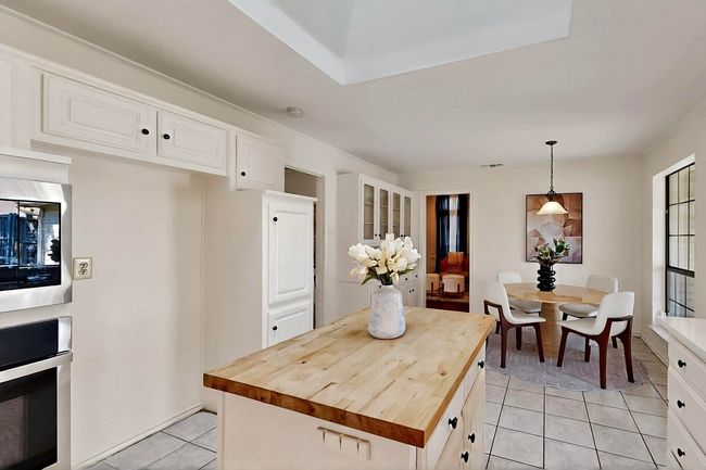 Kitchen featuring butcher block countertops, light tile patterned floors, oven, white cabinets, and decorative light fixtures | Image 11