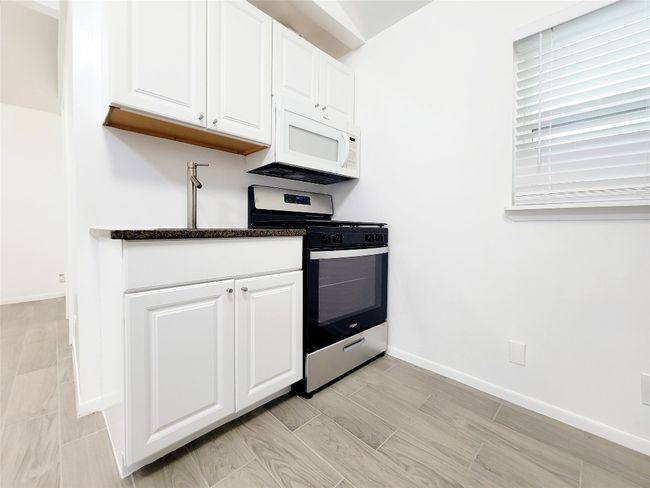 Kitchen with stainless steel gas stove, white cabinetry, white microwave, baseboards, and dark stone countertops | Image 7