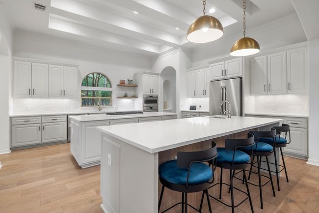 Kitchen featuring stainless steel appliances, a center island with sink, a tray ceiling, arched walkways, and crown molding | Image 9
