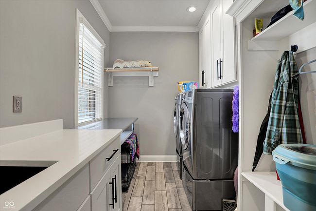 clothes washing area with crown molding, wood finish floors, cabinet space, baseboards, and independent washer and dryer | Image 18