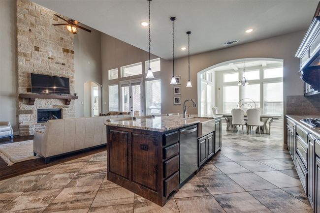 Kitchen featuring dark brown cabinets, a center island with sink, stainless steel dishwasher, plenty of natural light, and a fireplace | Image 11