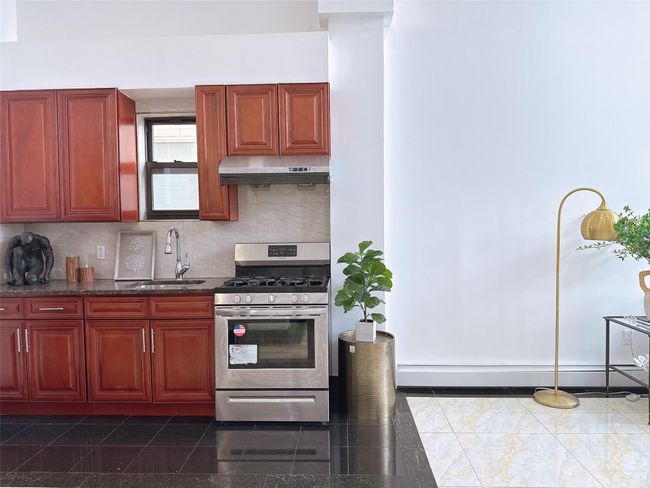 Kitchen with stainless steel gas range, reddish brown cabinets, a baseboard heating unit, and backsplash | Image 5