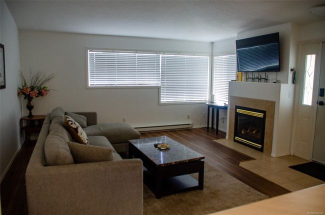 Living room featuring a baseboard radiator, plenty of natural light, a tiled fireplace, and wood finished floors | Image 17