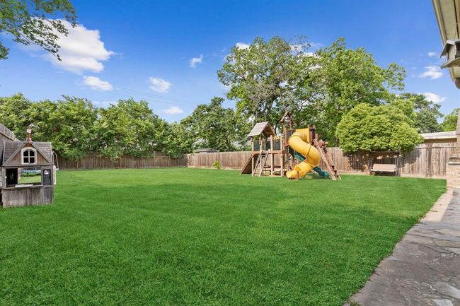 Spacious backyard with lush green lawn, mature trees, children's playset, and a charming playhouse, perfect for family outdoor activities. | Image 36