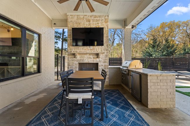 View of patio / terrace with an outdoor stone fireplace, exterior kitchen, fence, a ceiling fan, and a grill | Image 34