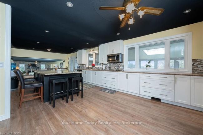 Kitchen with white cabinets, a center island, light stone countertops, and a breakfast bar area | Image 12