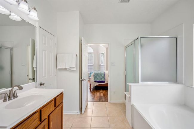 Exiting the second doorway, you get a view back toward the bedroom. The soaking tub and separate shower sit to the right, creating a relaxing retreat just steps from the spacious primary suite. | Image 21