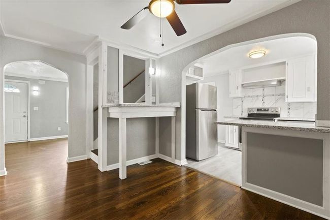 Kitchen with stainless steel appliances, arched walkways, a ceiling fan, wood finished floors, and light stone countertops | Image 10