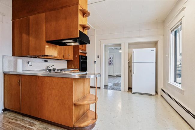 Kitchen with a healthy amount of sunlight, a baseboard heating unit, black oven, white fridge, and stainless steel counters | Image 12