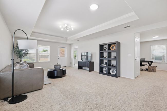 Carpeted living room and dining room with an inviting chandelier, a tray ceiling, and ornamental molding | Image 7