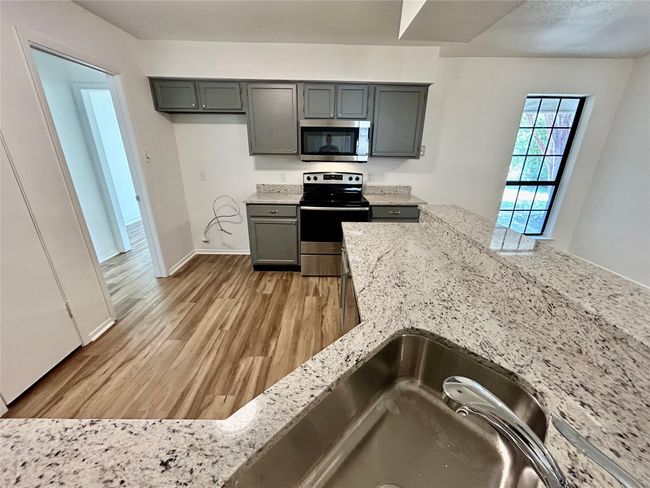 Kitchen with stainless steel appliances, light wood-style floors, light stone counters, baseboards, and gray cabinets | Image 9