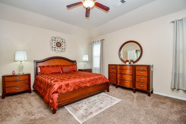 Cozy master bedroom with a warm color scheme features a spacious bed, elegant wooden furniture, and soft carpeting. | Image 15