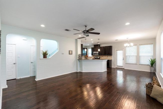 Unfurnished living room with a ceiling fan, a chandelier, dark wood finished floors, recessed lighting, and arched walkways | Image 6