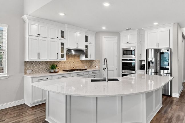 Kitchen featuring decorative backsplash, glass insert cabinets, white cabinets, appliances with stainless steel finishes, and recessed lighting | Image 6