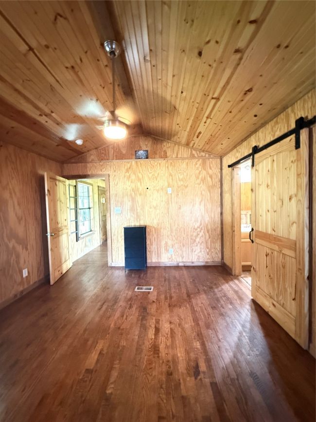 Unfurnished living room with a barn door, vaulted ceiling, wooden walls, dark wood-type flooring, and wood ceiling | Image 9