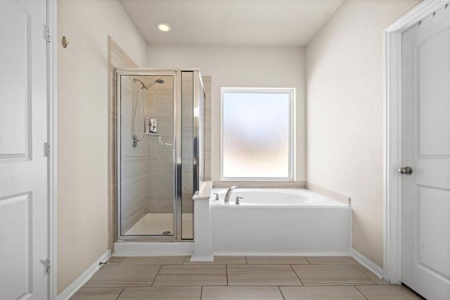 This primary bathroom features a modern design with a spacious glass-enclosed shower and a separate bathtub. It has neutral tones, tiled flooring, and a large frosted window for natural light while maintaining privacy. | Image 18