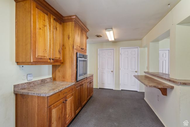 Kitchen with stainless steel oven, dark colored carpet, and brown cabinets | Image 12